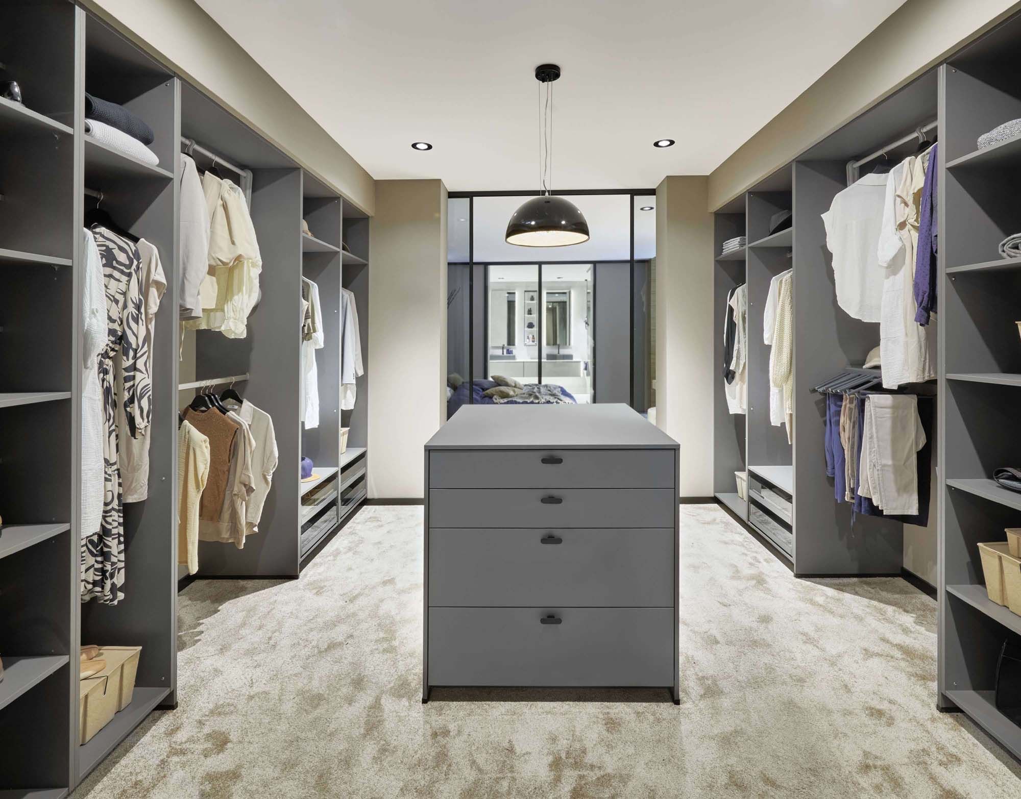 Eleganter begehbarer Kleiderschrank mit symmetrischer Raumaufteilung, offenen Schrankelementen und zentraler Kommode. Die maßgefertigte Raumplanung sort für optimale Übersicht, viel Strauraum und eine ruhige Atmosphäre.