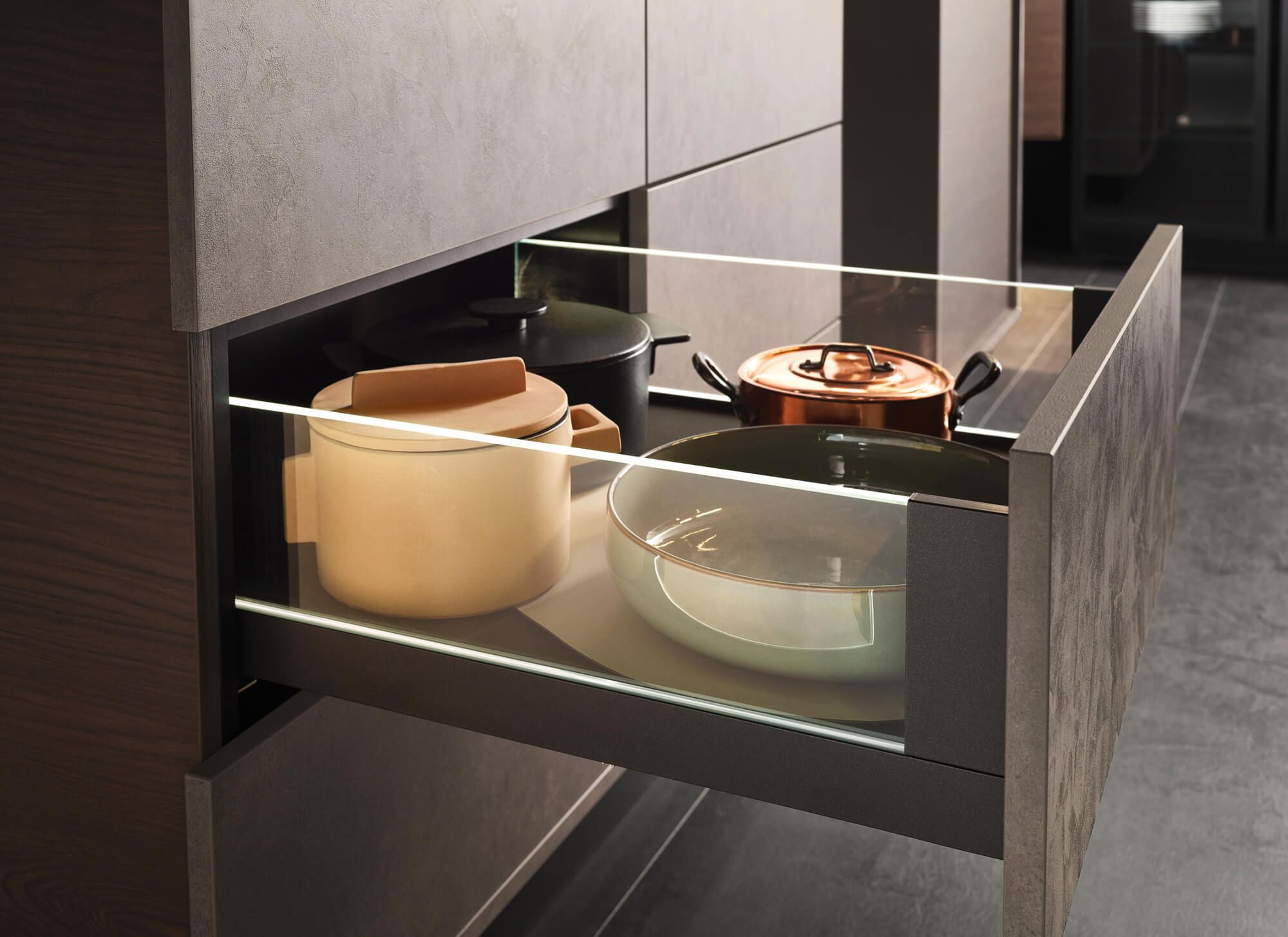 Offene Küchenschublade mit verschiedenen Kochtöpfen und Glasfront in moderner Küche