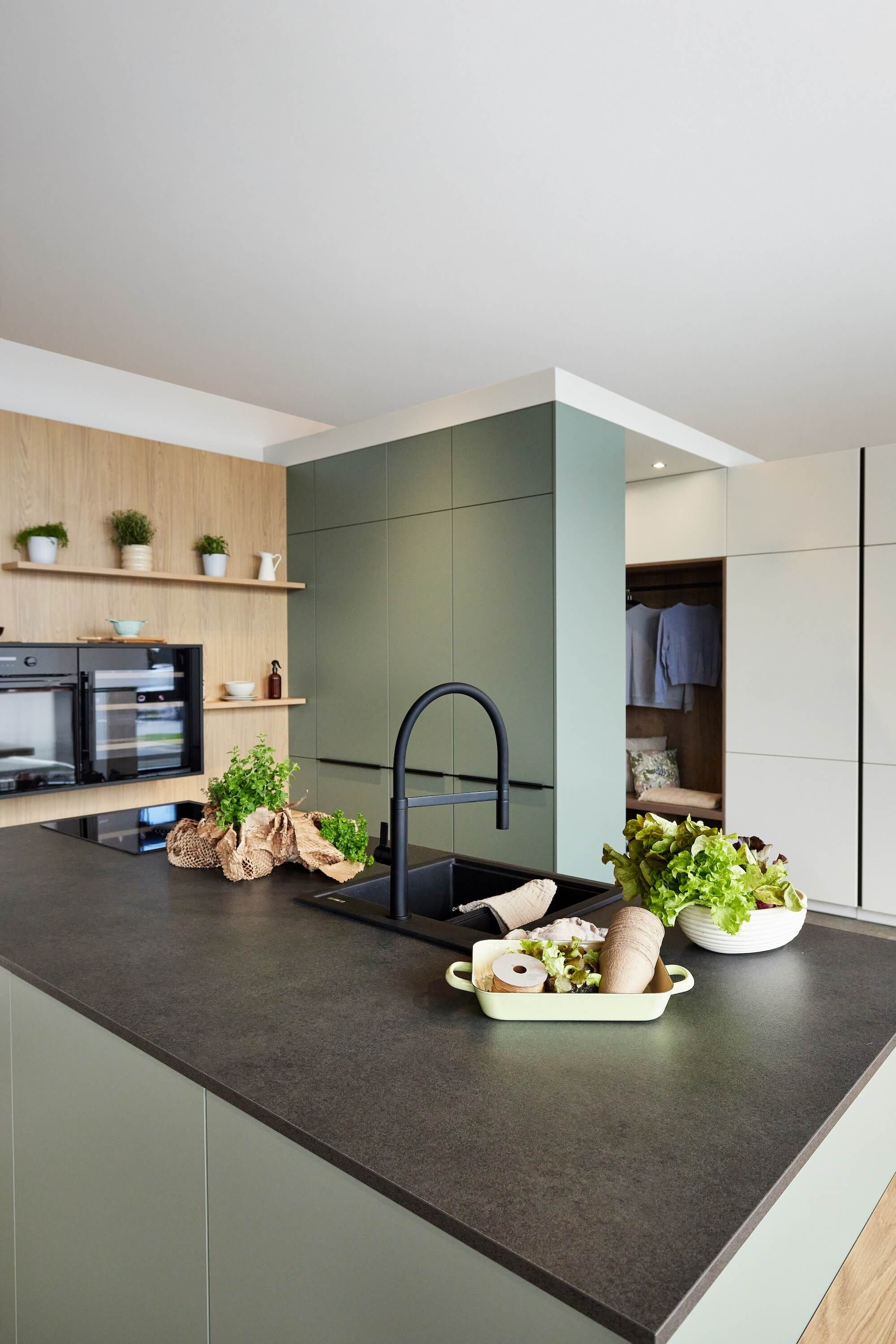Elegante, grüne DAN Küche mit schwarzen Geräten und schwarzer Spüle und Armatur.