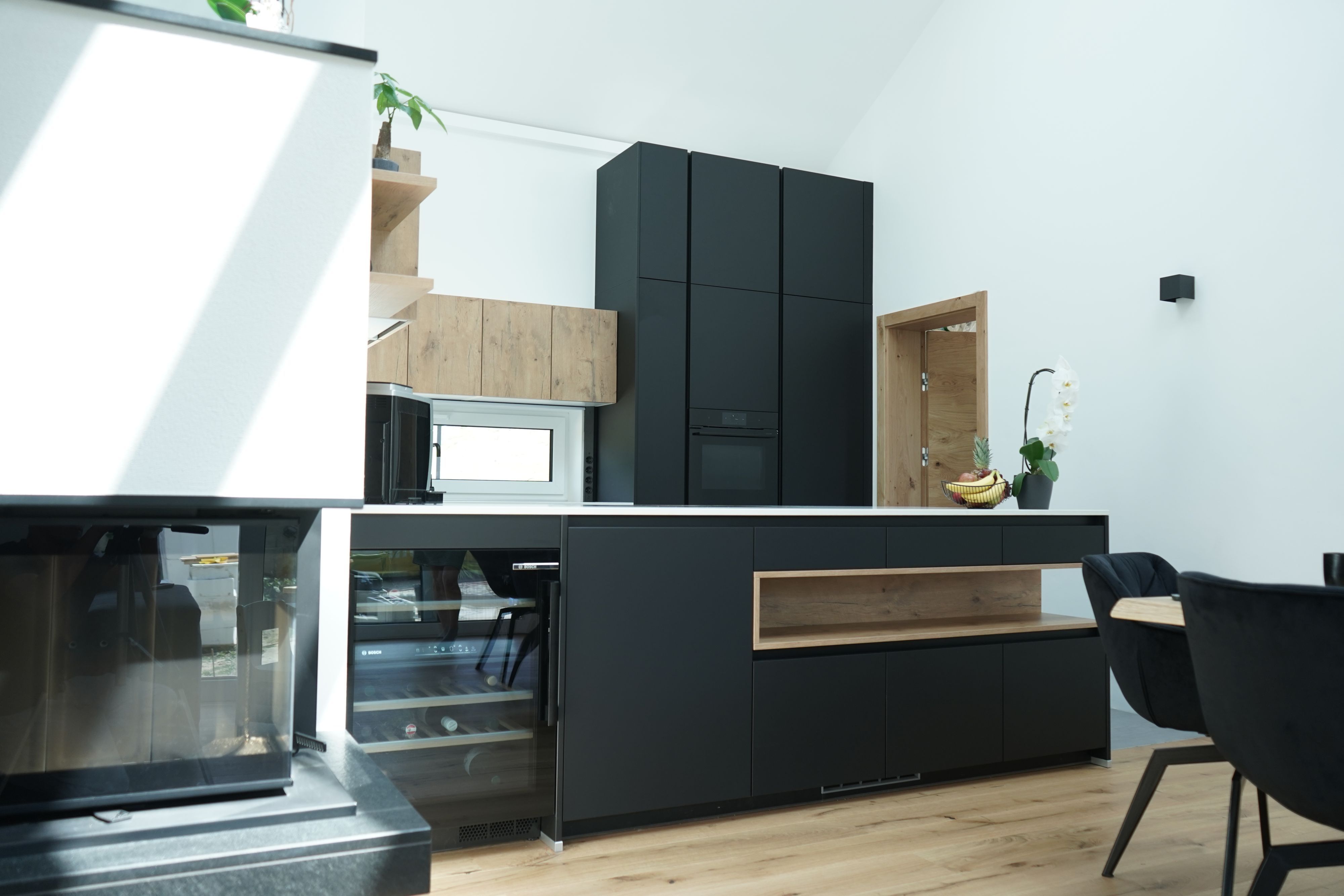 Stilvolle Grifflose Küche mit Kücheninsel in Schwarz und Holz, klarer Lienienführung und integrierten Stauraumlösungen.