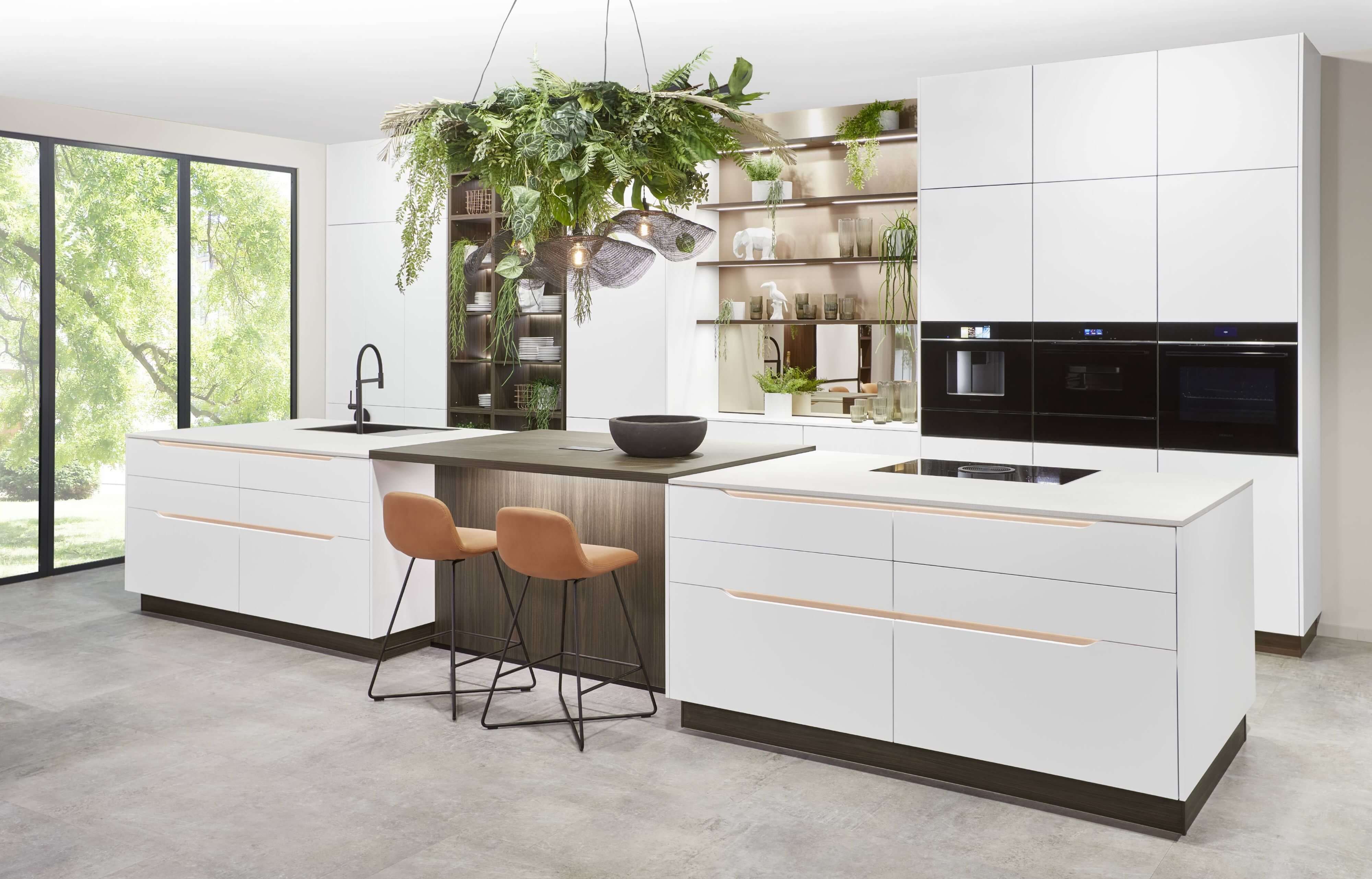 Große, moderne Küche mit Kochinsel und grifflosen Fronten in weiß matt. Die dunkle Arbeitsplatte und die Regale setzen einen eleganten Konstrast.