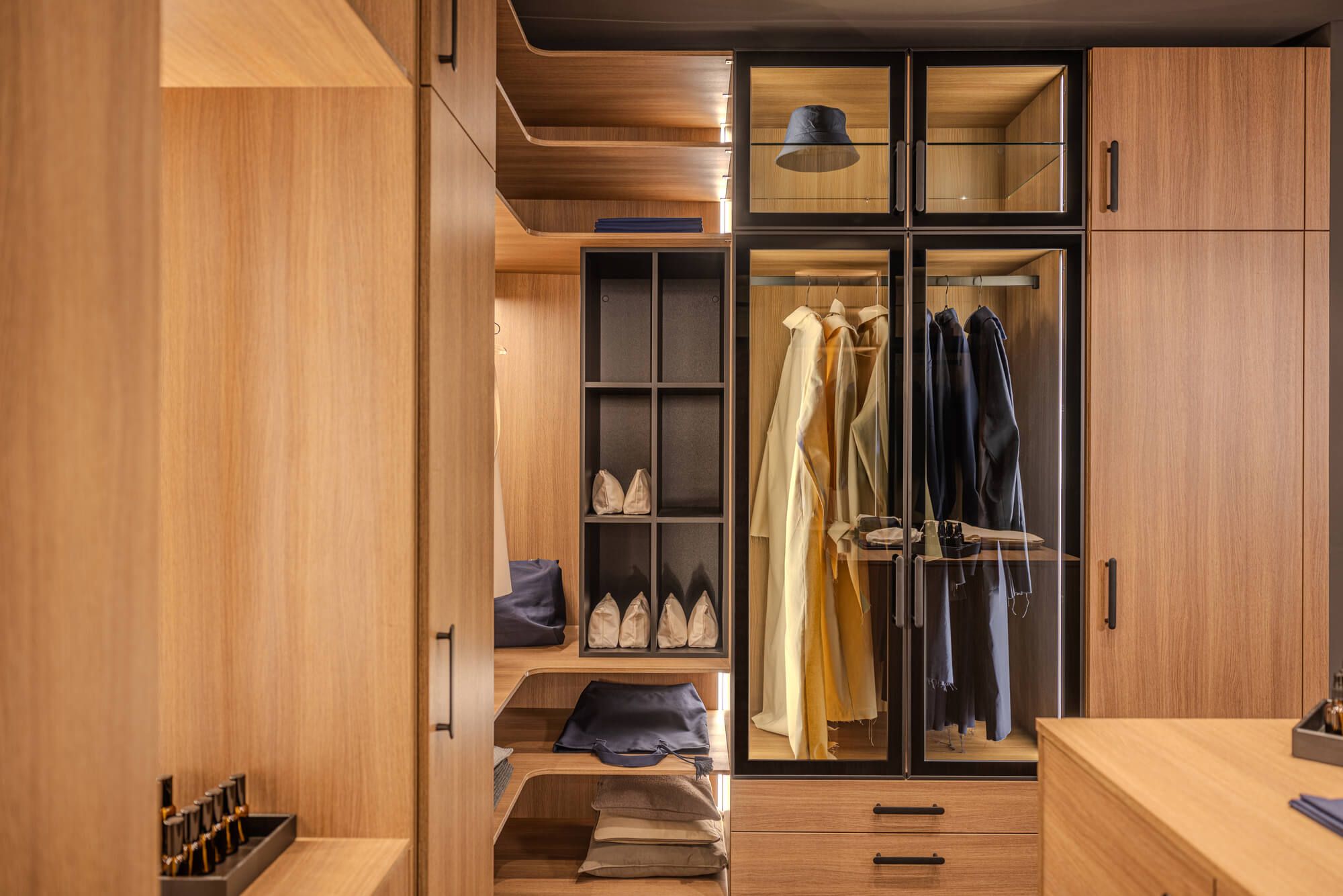 Geräumige Ankleide mit Holzschränken, Glastüren, geordneten Kleidungsstücken und Accessoires